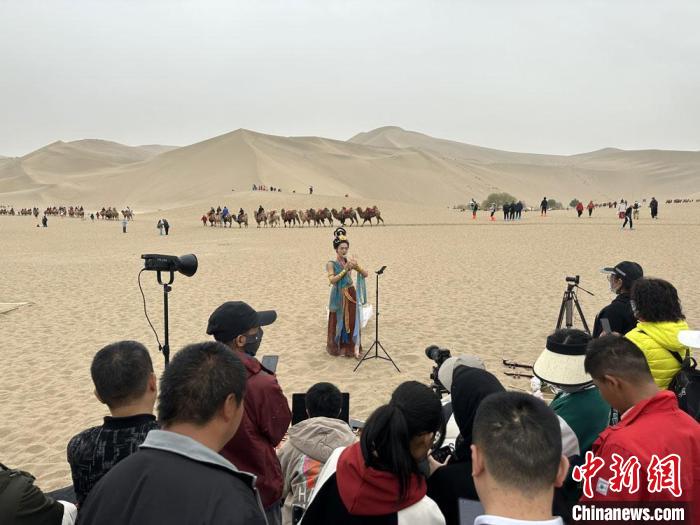 圖為2023年4月底，敦煌大漠“逐舞者”奧楠在鳴沙山月牙泉景區(qū)視頻直播，吸引游人圍觀?！●T志軍 攝